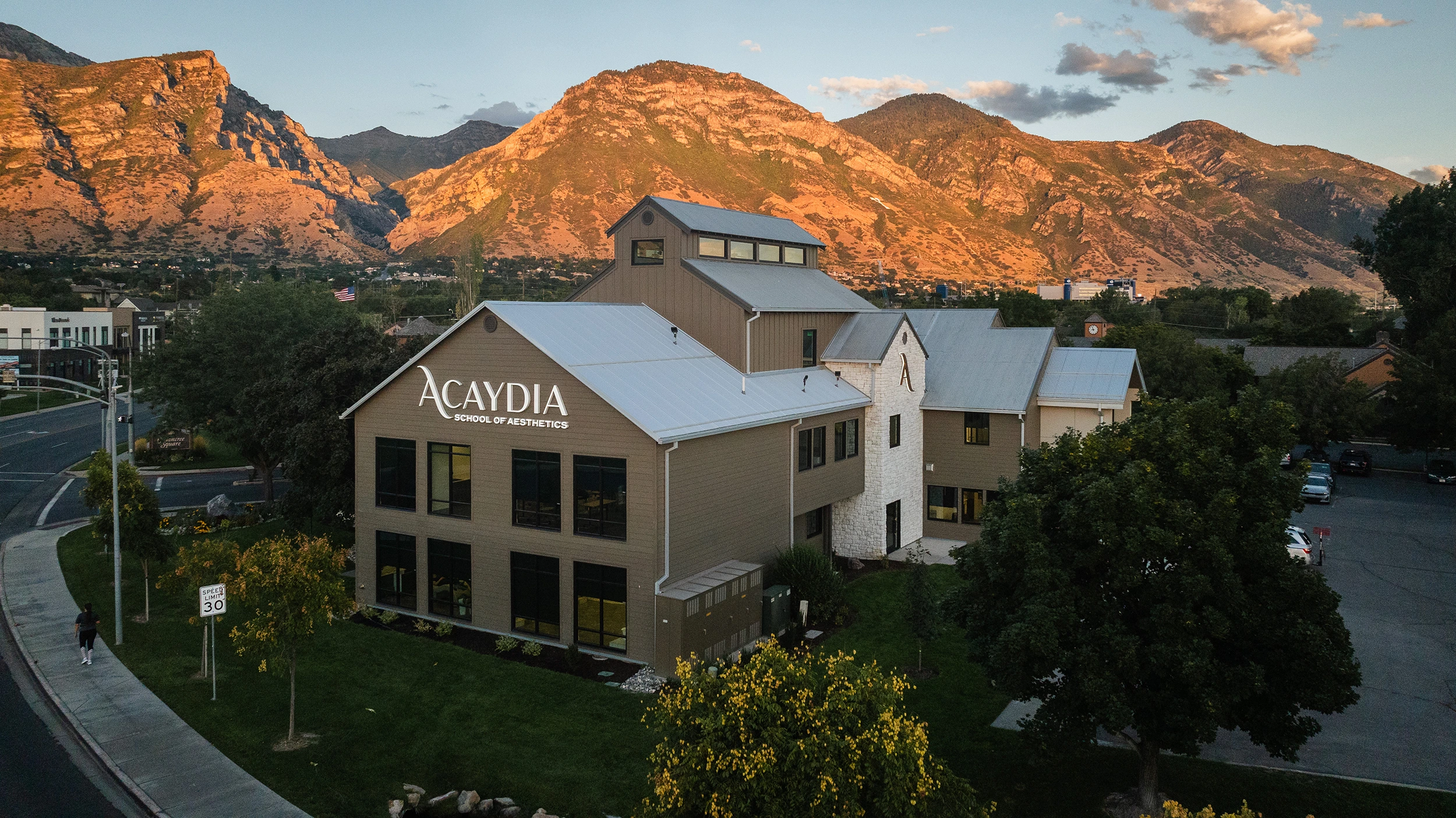 The Acaydia School of Aesthetics campus in Provo, Utah, with the Wasatch mountains behind it at sunset